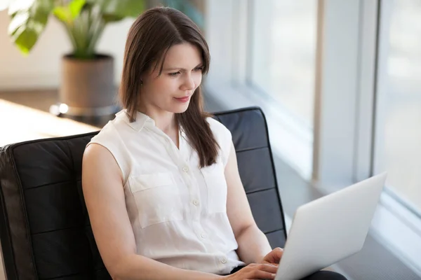 Успешная женщина занята работой за ноутбуком, сидя в кресле — стоковое фото