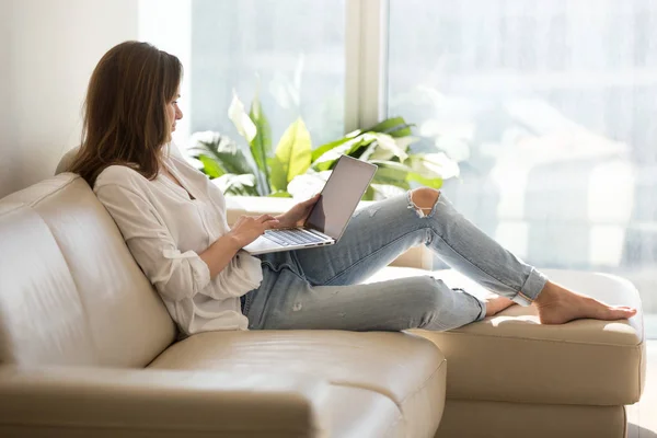 Feliz feminino navegação internet sentado no sofá em casa — Fotografia de Stock