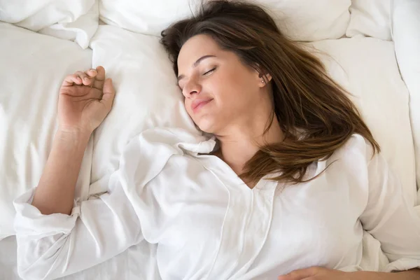 Расслабленная молодая женщина хорошо спит в уютной белой кровати — стоковое фото