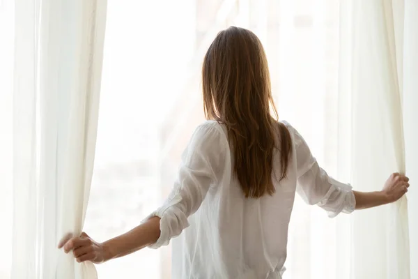 Gelukkige vrouw zoekt vanuit venster genieten van uitzicht op de stad ochtend — Stockfoto