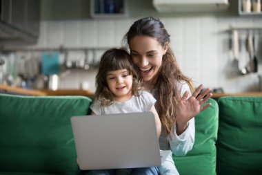 Mutlu anne ve çocuk kızı sallayarak eller dizüstü kullanarak web kameraya bakarak görüntülü görüşme, gülümseyen anne ve çocuk kız eğlenmek için online bilgisayar web kamerası uygulaması aracılığıyla videocall yapım tarafından tebrik