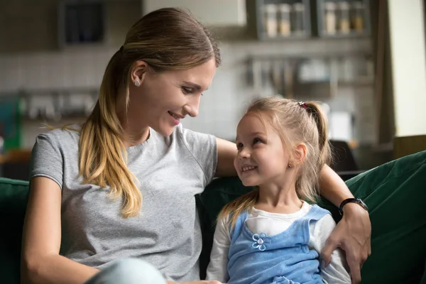 Sonriente niña hija mirando amorosa madre abrazándose en sofá — Foto de Stock