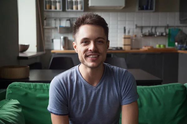 Sorrindo homem olhando para a câmera sentado no sofá da cozinha, retrato — Fotografia de Stock