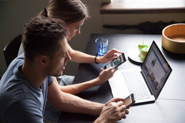 Молодая пара одержима смартфонами и ноутбуками, проверяющими onlin
