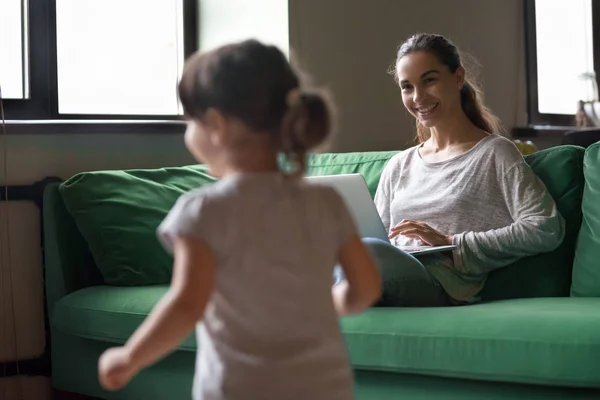 Madre trabajando en el ordenador portátil mientras niña jugando en casa —  Fotos de Stock