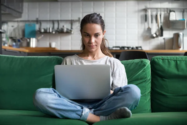 Serious woman using laptop checking news online sitting on sofa — Stock Photo, Image