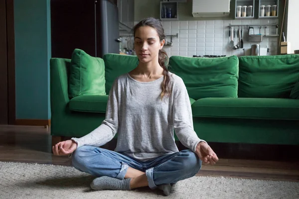 Calm woman sitting in lotus pose practicing meditation at home