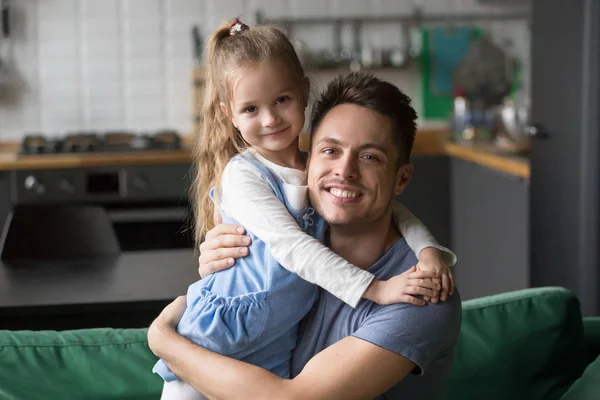 Portrait of happy dad hugging kid daughter looking at camera