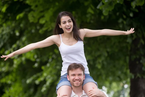 Opgewonden vriendin zitten op vriendje schouders uitrekkende handen — Stockfoto