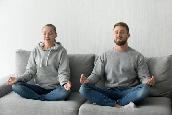 Calm couple meditating practicing yoga on couch together — Stock Photo, Image