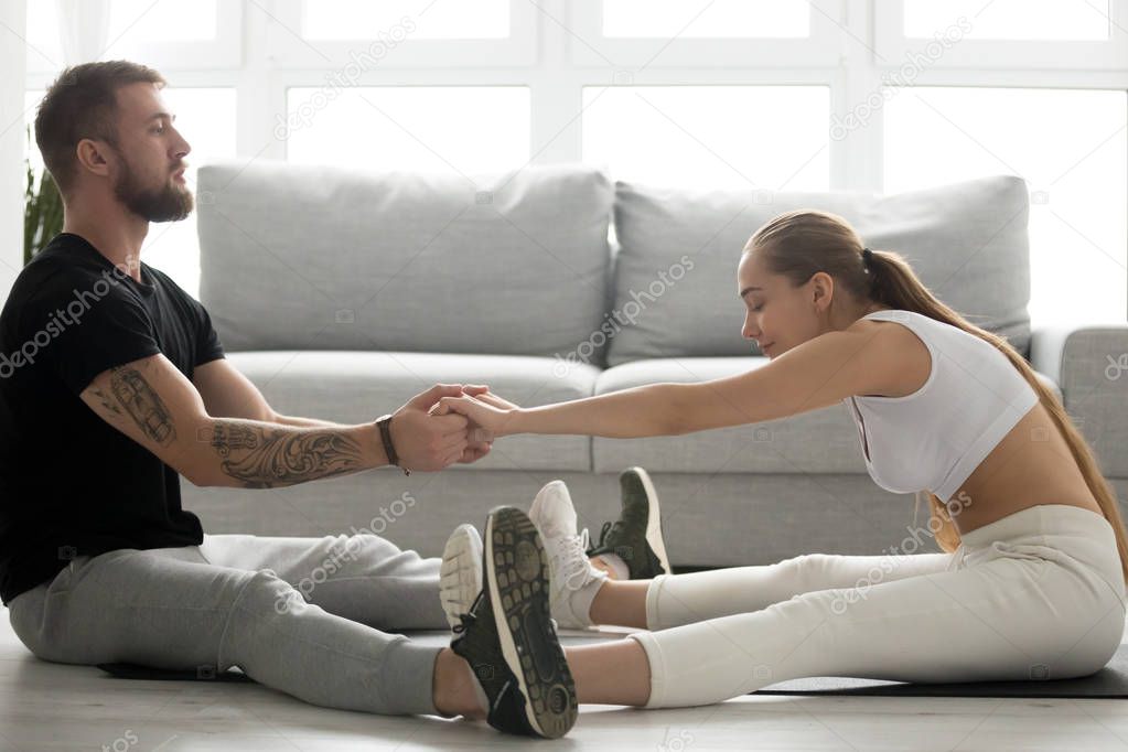 Toned man helping girlfriend stretch back after training