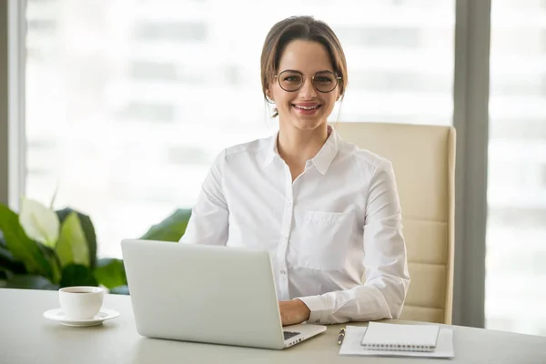 Mujer de negocios milenaria sonriente sentada en el escritorio con lapto — Foto de Stock