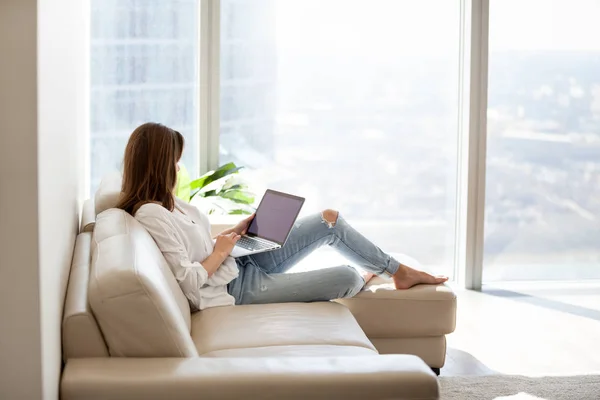 Relaxed woman using laptop sitting on sofa at luxury home