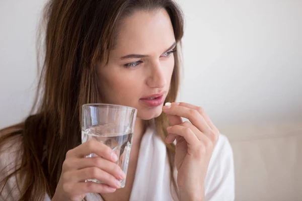 Doubtful woman holding pill and glass of water taking medicine — Stock Photo, Image