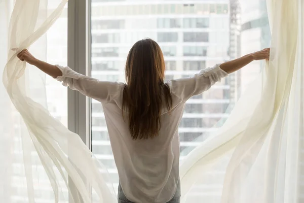 Tampilan belakang pada wanita membuka tirai jendela merasa bebas independen — Stok Foto