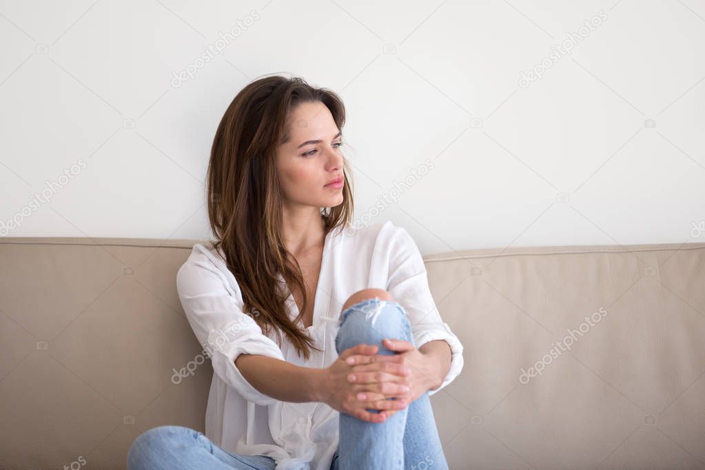 Thoughtful pensive millennial woman sitting on sofa feeling lone