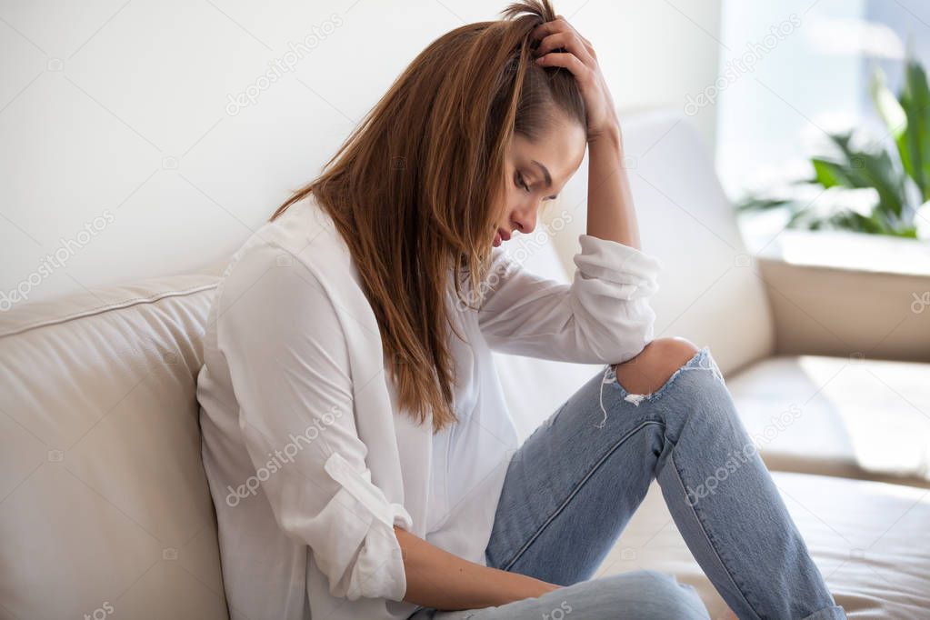 Sad depressed woman feeling bad at home sitting on sofa