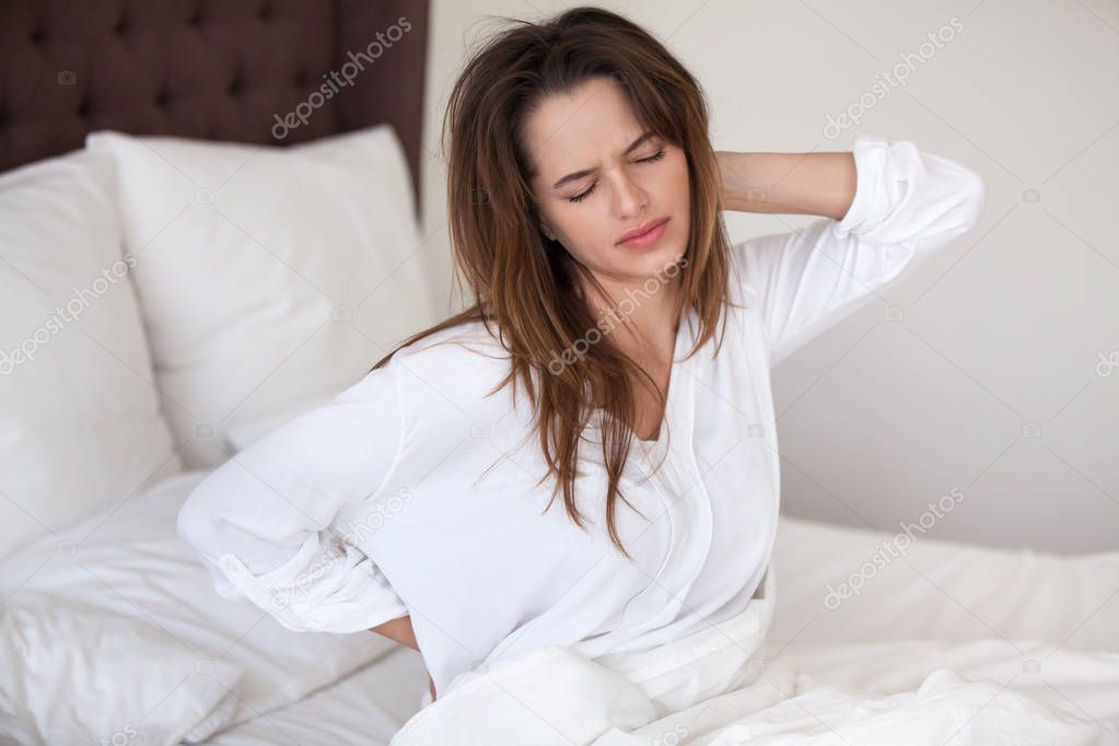 Unhappy woman waking up in bed feeling neck back pain