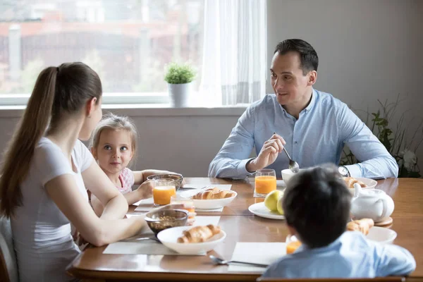 Happy parents with two kids enjoy healthy breakfast at home