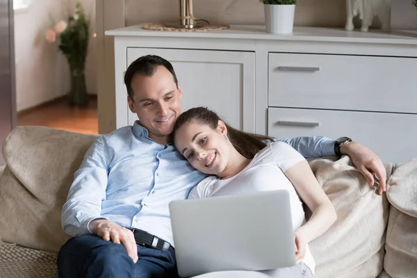 Loving couple cuddle on couch watching video on laptop