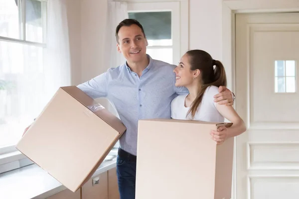 Excited couple holding cardboard boxes entering own house