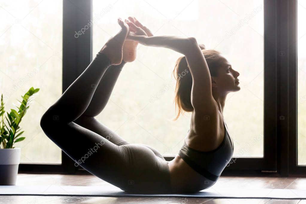 Young sporty attractive woman doing Dhanurasana exercise