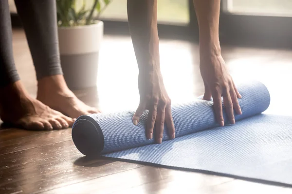 Woman unrolling blue yoga mat, legs close up