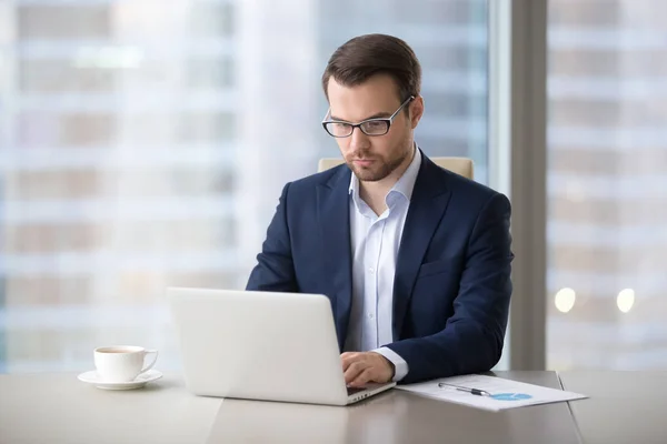 Serious businessman working typing letter on laptop