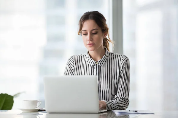 Empresária séria trabalhando on-line usando laptop no escritório — Fotografia de Stock