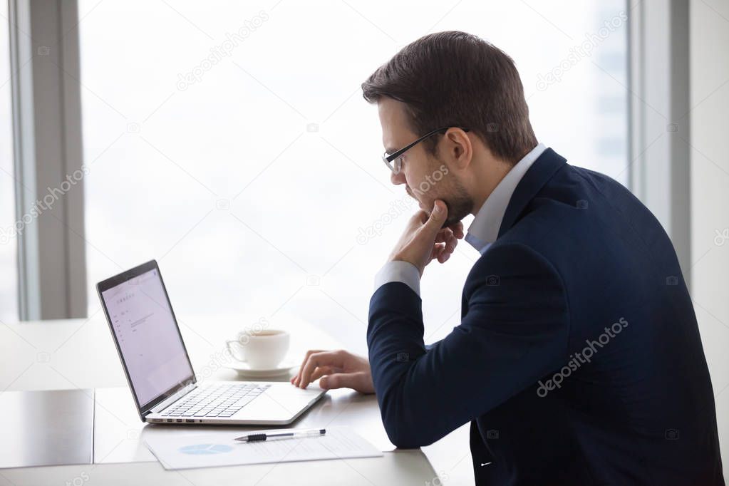 Thoughtful businessman writing business email on laptop