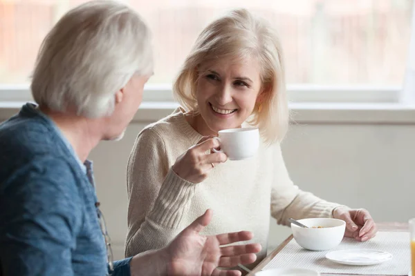 Sonriente mujer madura bebiendo café escuchando a un anciano hombre ta —  Fotos de Stock