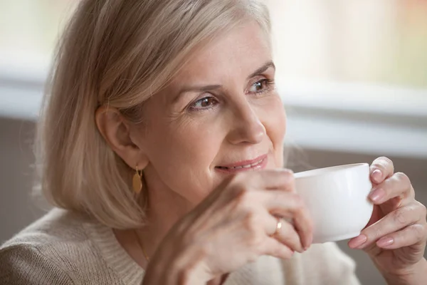 Задумчивая, улыбающаяся женщина средних лет, отводящая взгляд от мечтательного напитка — стоковое фото