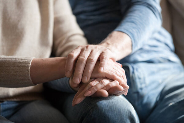 Closeup view of mature couple holding hands giving psychological