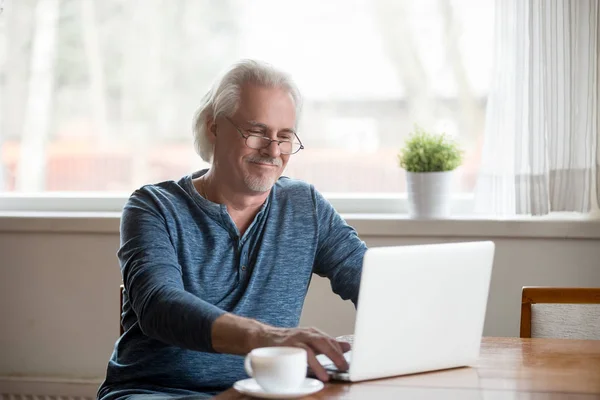 Lachende senior man in glazen werken op laptop thuis — Stockfoto