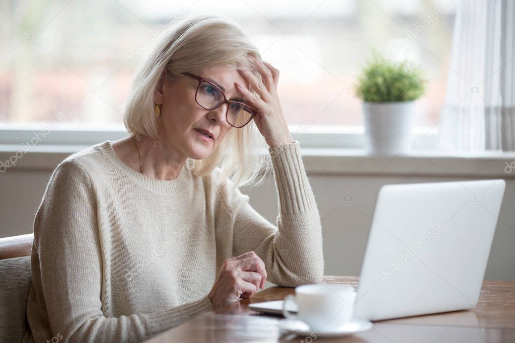 Confused mature woman thinking about online problem looking at l