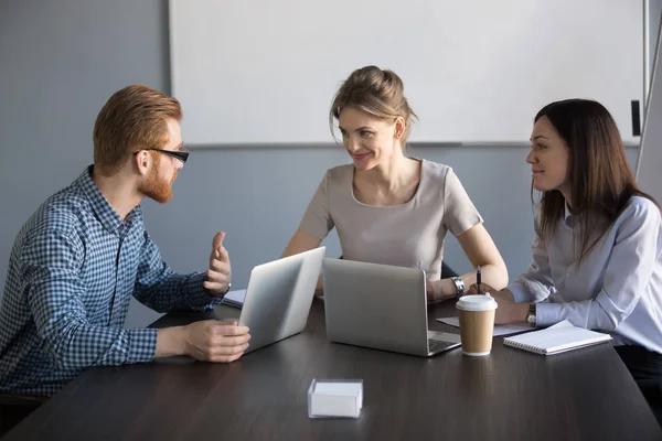 Mannlig kollega som forklarer smilende kvinnelige medarbeidere prosjektplan – stockfoto