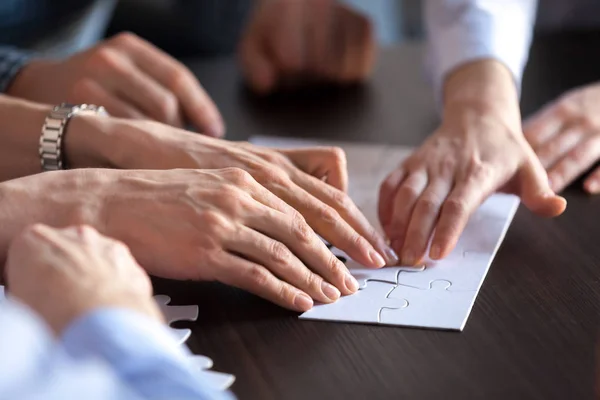 Hands connecting puzzle together on office desk, close up view — Stock Photo, Image