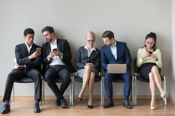 Diverse work candidates sit in queue using gadgets before interv