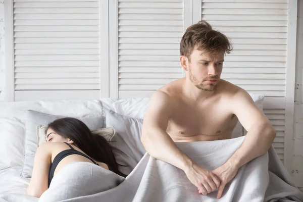 Разочарованный мужчина и спящая женщина лежат в постели — стоковое фото