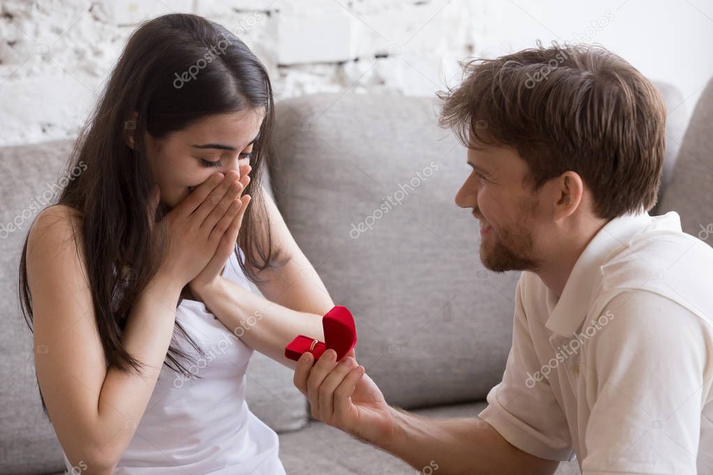 Happy young man propose to his girlfriend sitting on sofa