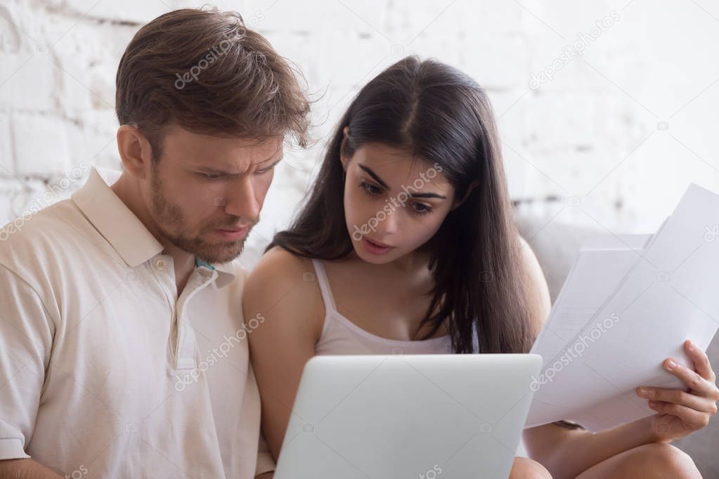 Frustrated young couple sitting on couch checking bills