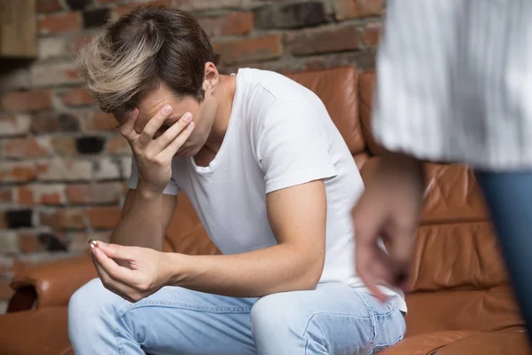 Sad man sitting on couch with engagement ring