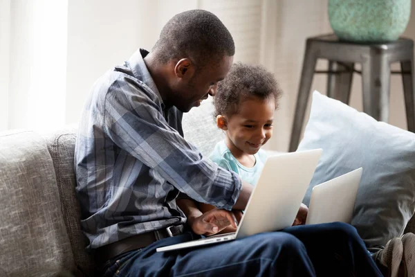 Padre con hijo pequeño usando computadoras sentadas en el sofá —  Fotos de Stock