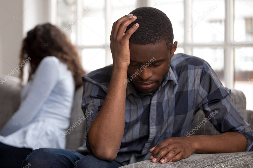 Unhappy black married couple sitting on couch at home