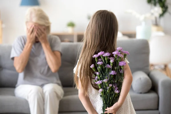 Ragazzina che fa sorpresa per la nonna che tiene i fiori — Foto Stock