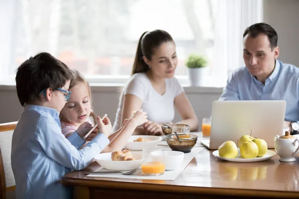 Familia con niños usando aparatos sentados en la mesa de comedor — Foto de Stock
