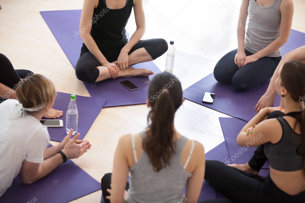 Sporty people sitting in a circle during yoga seminar