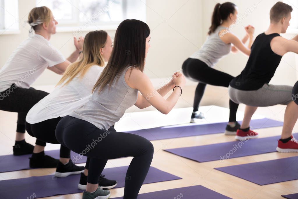 Sportive girls and guys doing crouching at gym