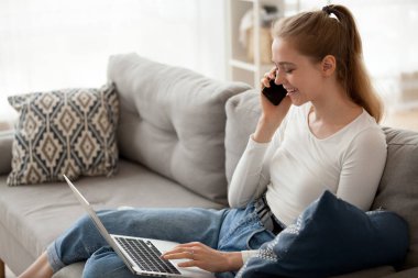 Telefonla konuşurken dizüstü kullanarak kanepede oturan kadın