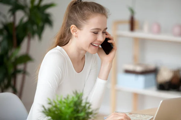 Young woman sitting at the desk talking by mobile phone — Stock Photo, Image